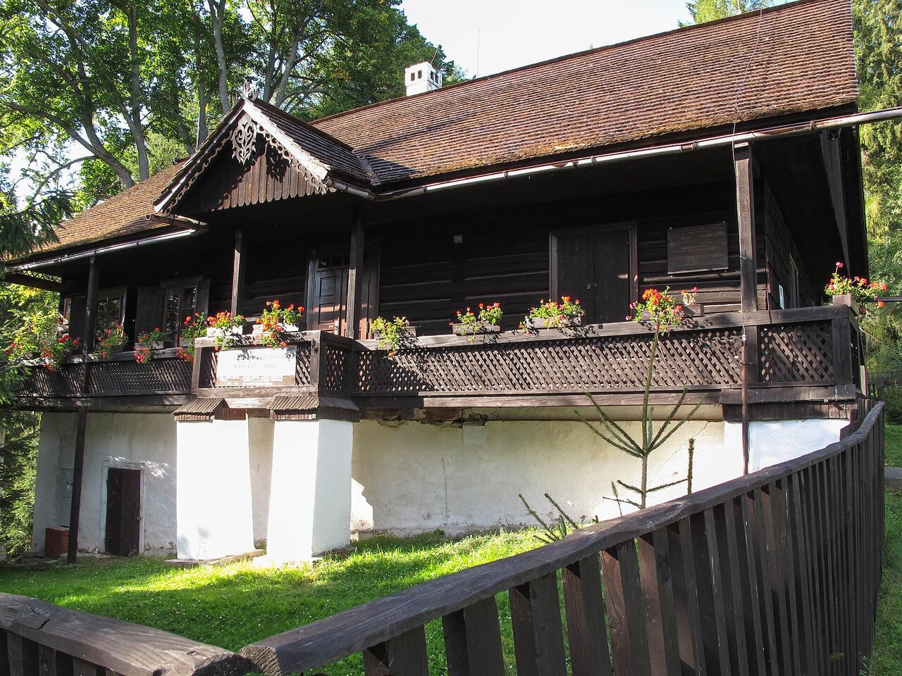 Tradičný drevený dom s pavlačou zdobenou kvetmi a šindľovou strechou